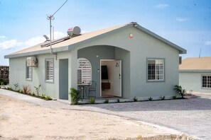 A single-story building with a flat roof, a satellite dish, and a small porch area with a chair. - Sunset@ArecaHomes ~ Beach Access~Pool & Water Park (Discovery Bay, St Ann)
