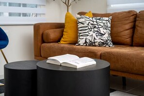 A brown leather sofa with a black and white patterned pillow, a yellow pillow, and a book on a black round table. - Sunset@ArecaHomes ~ Beach Access~Pool & Water Park (Discovery Bay, St Ann)
