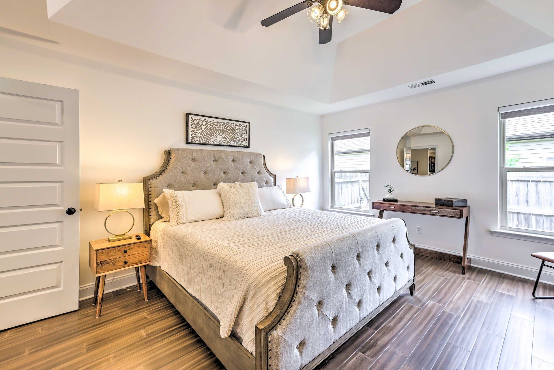 Une chambre à coucher avec un grand lit, une table de chevet, une commode, un ventilateur de plafond et une fenêtre avec des stores.