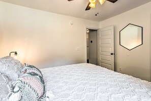 A bedroom with a white quilted bedspread, a patterned throw pillow, a ceiling fan, and a wall-mounted light fixture. - CLEAN Family-Friendly Getaway with Bonus Game Room! (Calera)