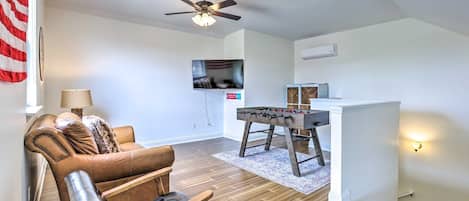 A living room with a leather sofa, a wooden coffee table, a ceiling fan, a television, and a foosball table.