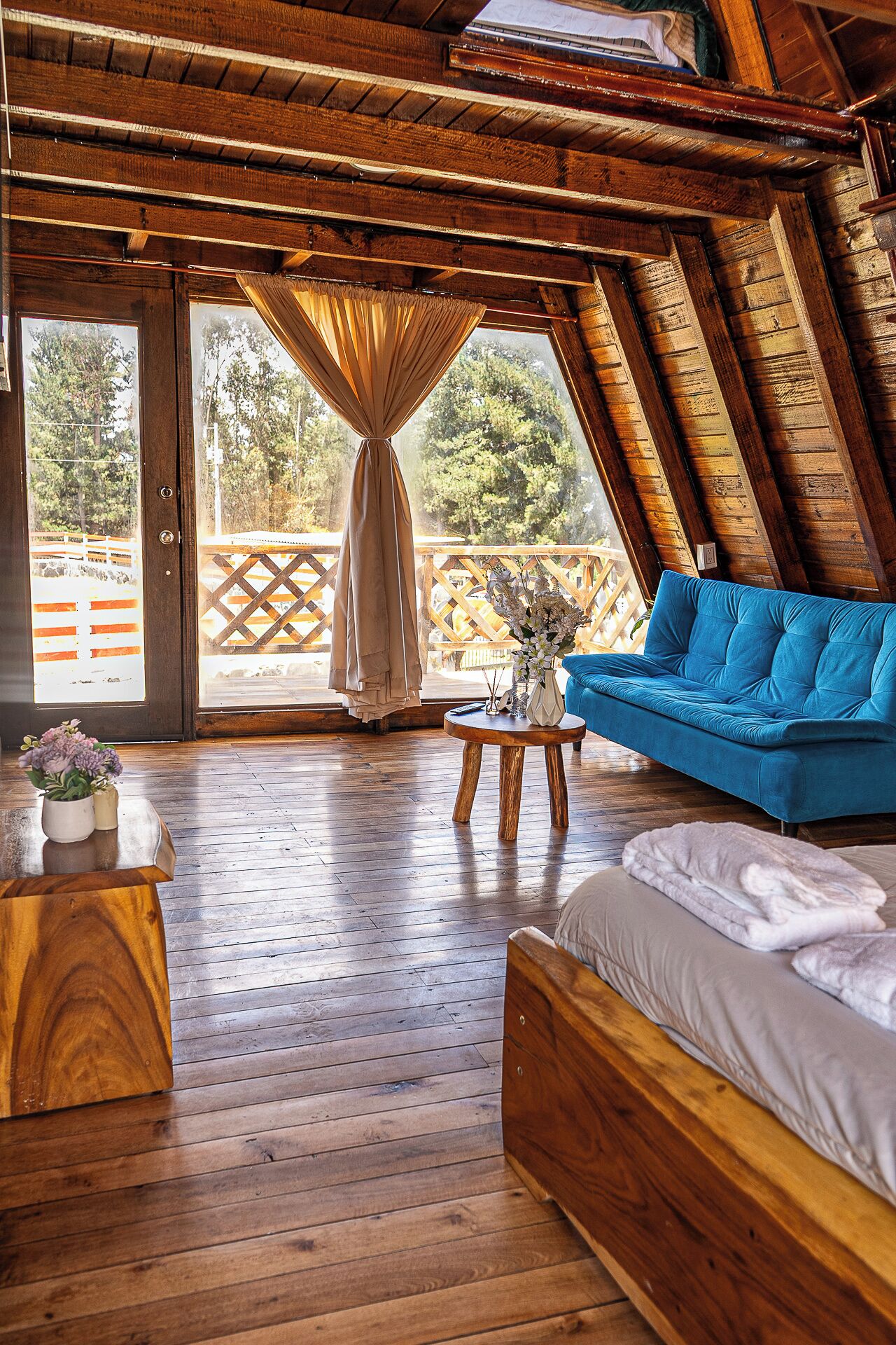 A cozy room with a wooden ceiling, a blue sofa, a wooden bed, and a wooden table with a vase of flowers.