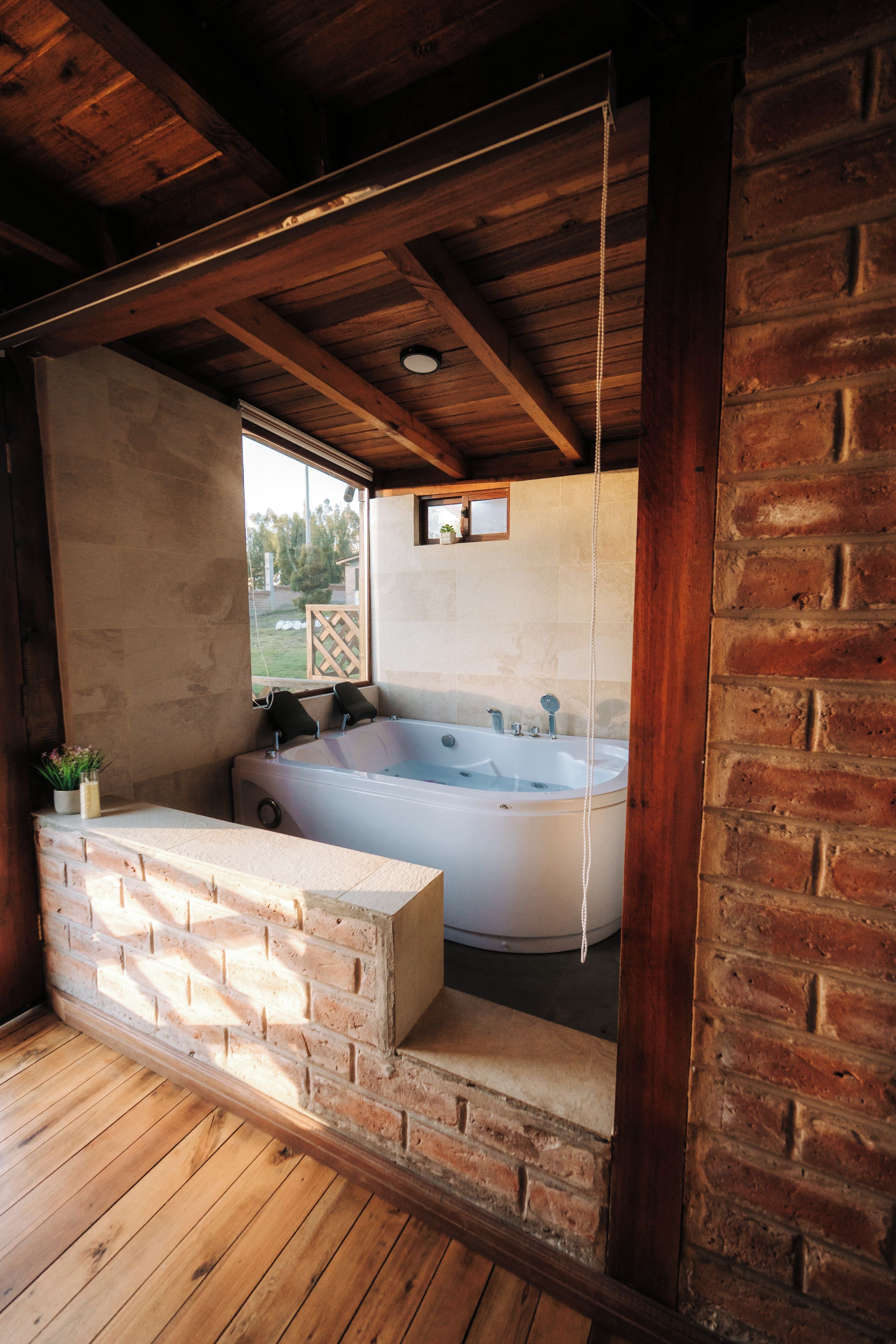 Une cabane en bois avec une grande baignoire, une fenêtre et un mur en briques.