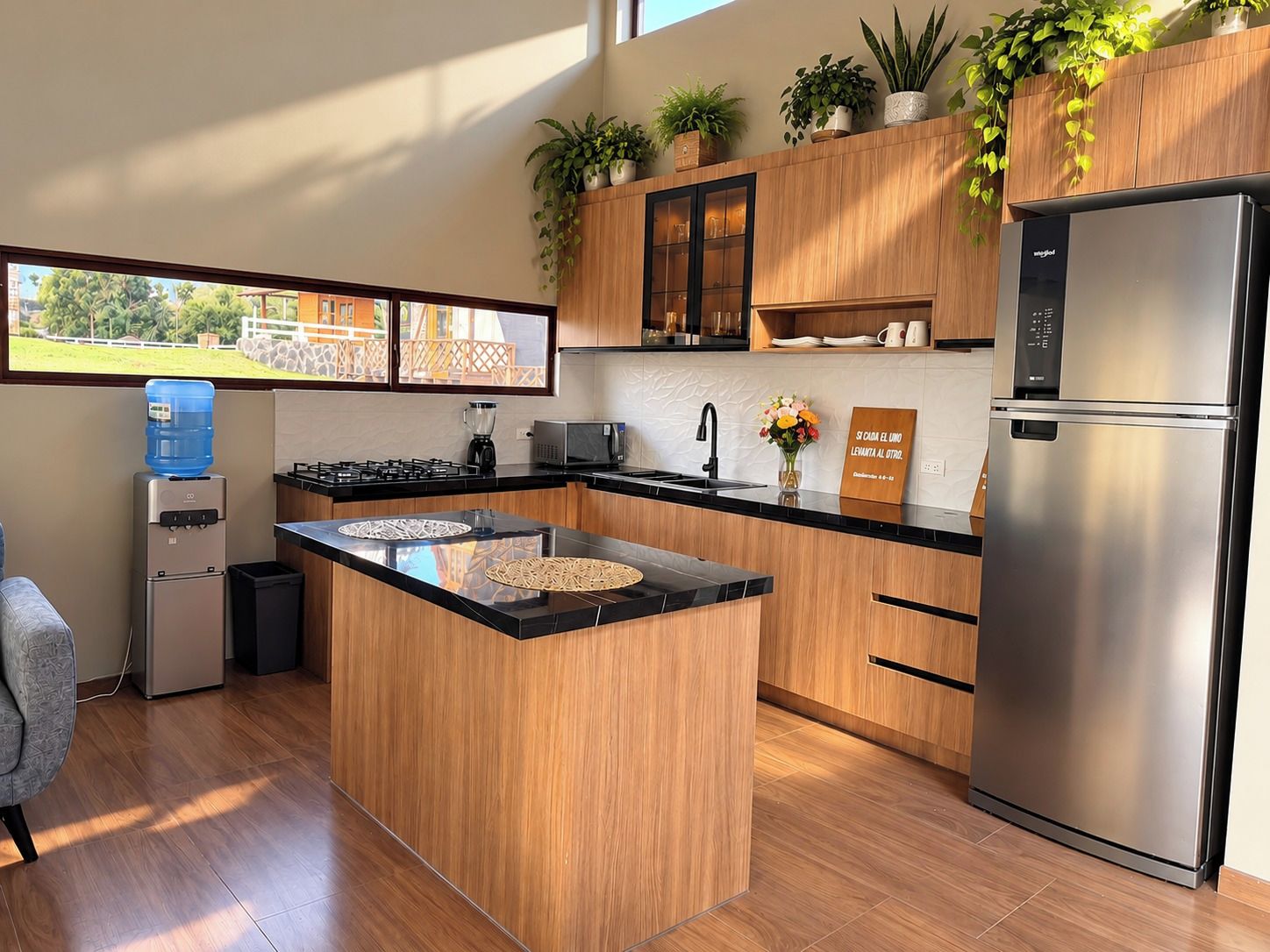 Une cuisine moderne dotée d’un îlot central, d’appareils électroménagers en acier inoxydable, de meubles de rangement en bois et d’un distributeur d’eau.