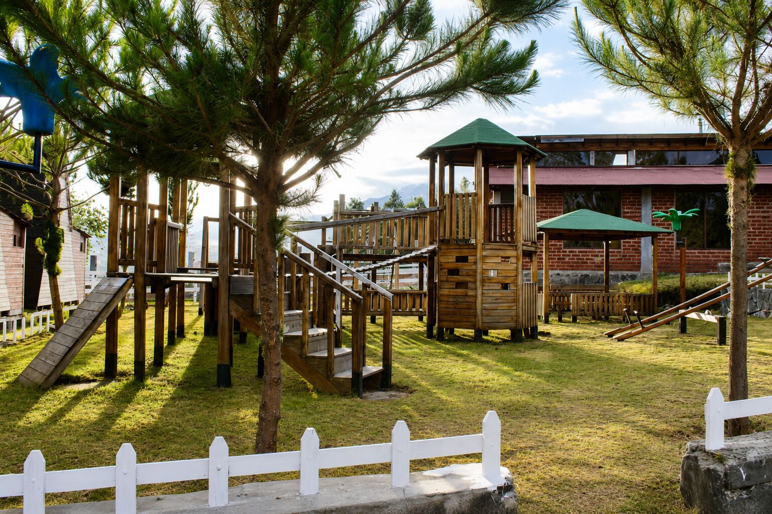 Un terrain de jeux avec des structures en bois et un bâtiment en briques en arrière-plan.