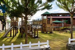 Un parque infantil con estructuras de madera y un edificio de ladrillo al fondo.