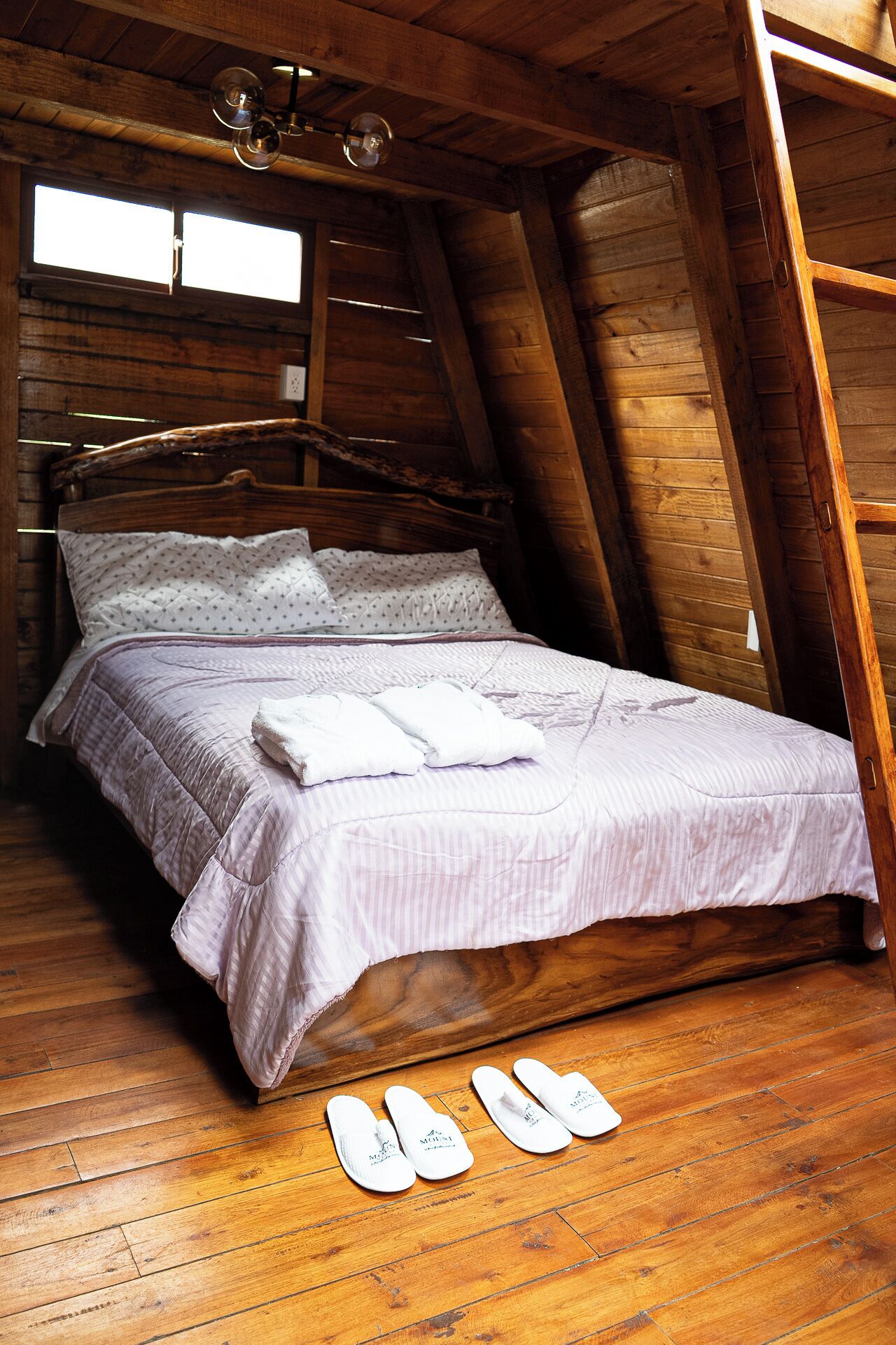Quarto com estrutura de madeira, uma cama, uma janela e piso de madeira.