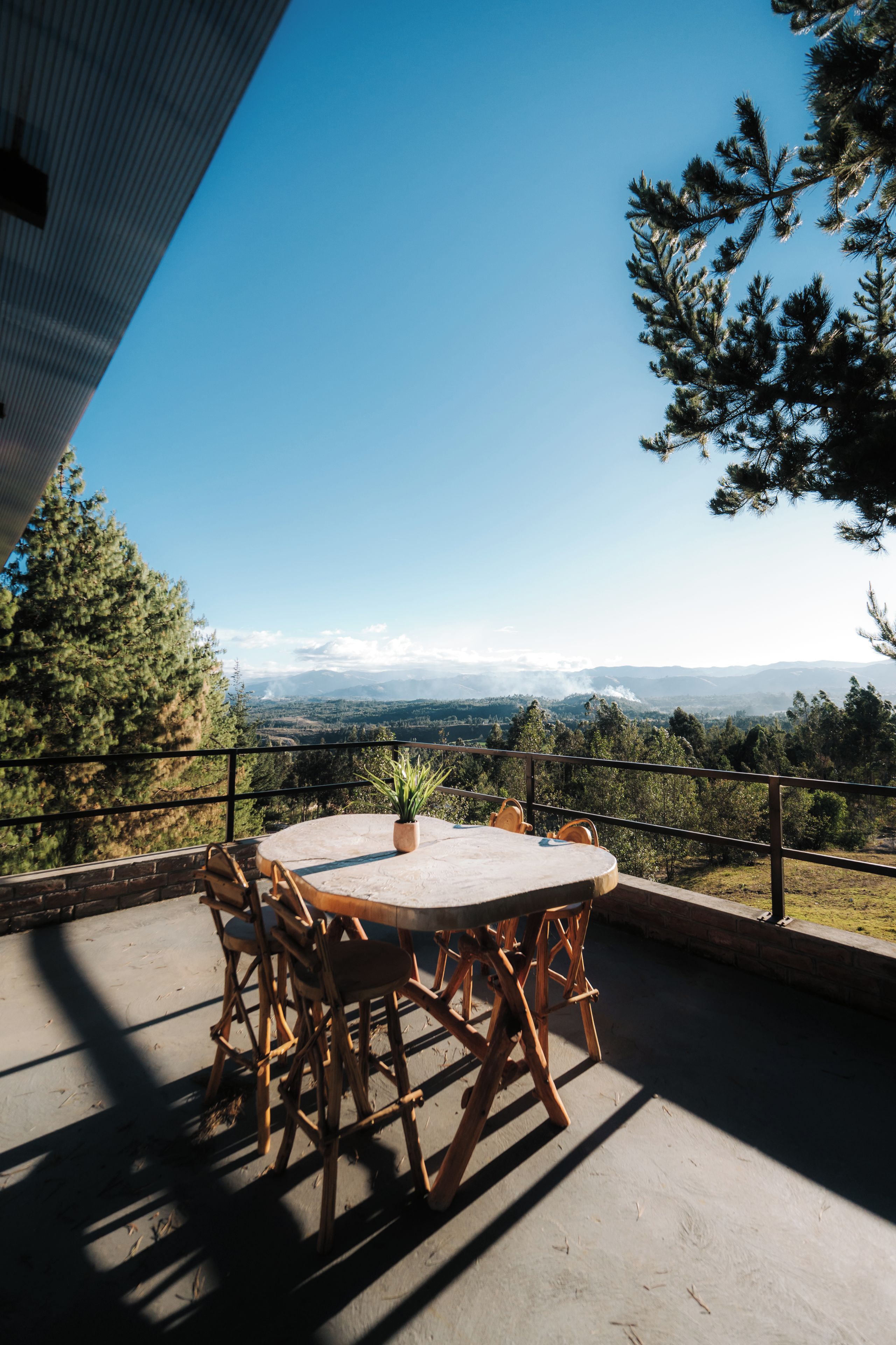 Un patio al aire libre con una mesa redonda y sillas, con vistas a un paisaje montañoso.