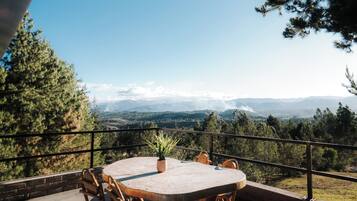 Un patio al aire libre con una mesa redonda y sillas, con vistas a un paisaje montañoso.
