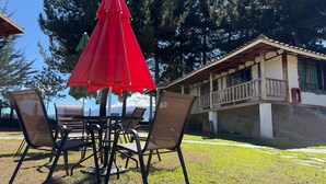 Un área de estar al aire libre con una mesa y sillas, un paraguas rojo y un edificio con balcón al fondo.
