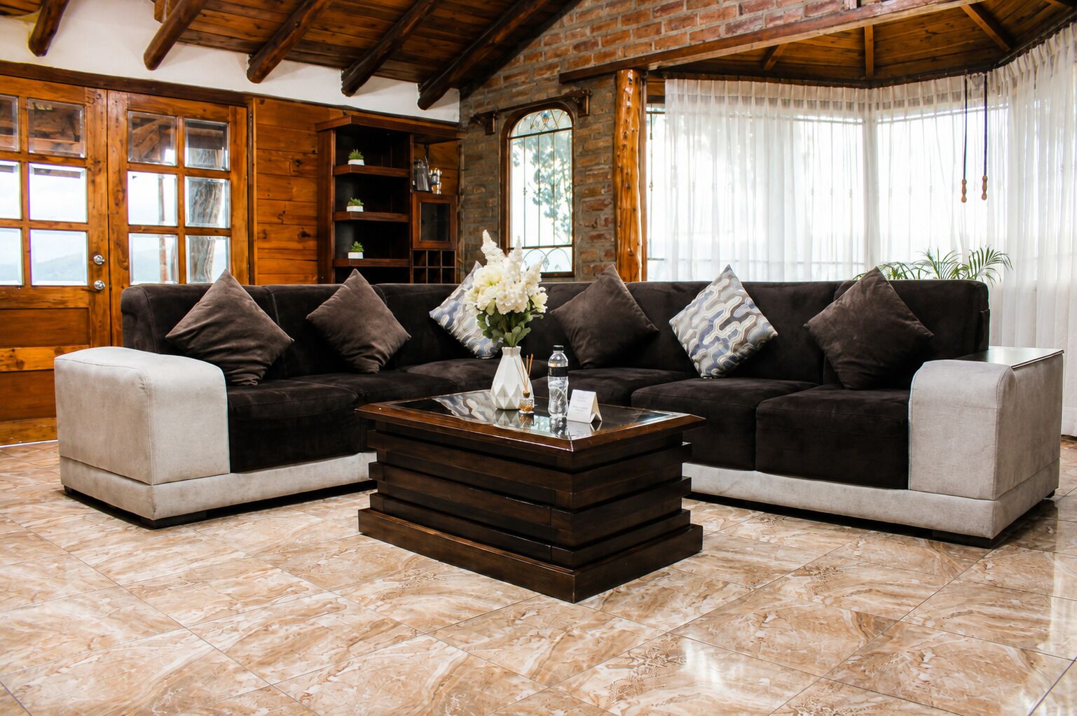 Una sala de estar con un sofá seccional marrón oscuro, un sillón blanco de acento y un mesita de centro de madera con un jarrón de flores.