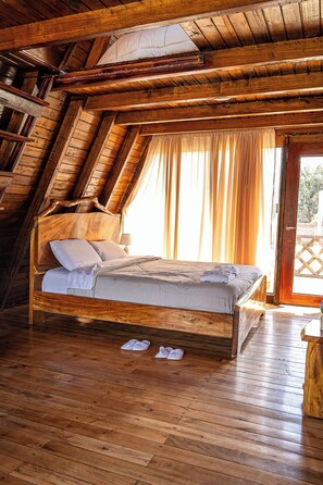 A wooden bed in a room with sloped ceilings and a view through a window.