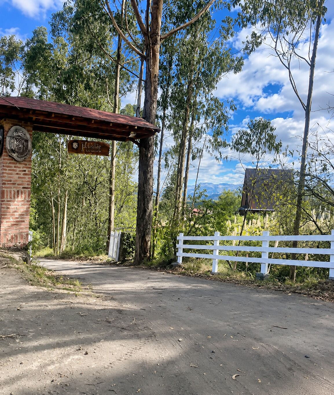 Una entrada rústica con un edificio de ladrillo, un letrero de madera y una cerca blanca.