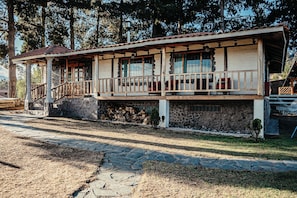 Un edificio de dos pisos con base de piedra, barandillas de madera en el balcón y una escalera que lleva al piso superior.