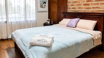 Habitación de hotel con cabecera de madera, cama con colcha azul claro y dos toallas con el nombre del hotel.