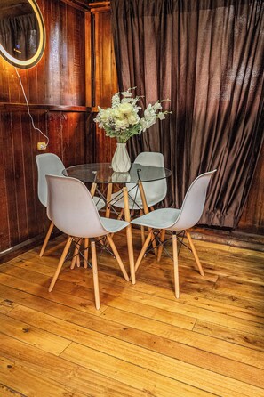 Un comedor con una mesa de madera, cuatro sillas, un jarrón con flores y un cortinero de fondo.