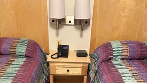 Camera d'albergo con due letti, un comodino con lampada, telefono e sveglia digitale.