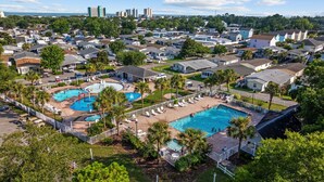 Zona residencial con varias piscinas, rodeada de casas y palmeras.