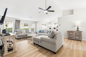 A spacious living room with a sofa, a coffee table, and a TV on a stand. - Newly remodeled 3BR/2BA Oceanfront Golf Cart Village Beach House (Surfside Beach)