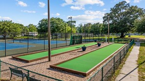 A tennis court with a green artificial turf area, surrounded by a fence and trees. - Newly remodeled 3BR/2BA Oceanfront Golf Cart Village Beach House (Surfside Beach)