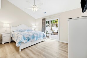 A bedroom with a bed, bedside tables, a ceiling fan, and a view through a window. - Newly remodeled 3BR/2BA Oceanfront Golf Cart Village Beach House (Surfside Beach)