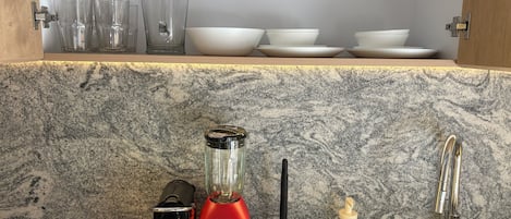Eine Küche mit einer Granitabdeckung, einem roten Mixer, einem schwarzen Entsafter, einer Spüle und einem Wasserhahn.
