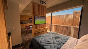 A bedroom with a bed, a TV mounted on a wooden wall, a wooden desk, and a view of a fenced outdoor area. - New, Fully Furnished Apartment in Guadalajara-Zapopan with AC and Pool—Pet-Friendly (Guadalajara)