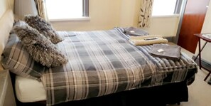 Een bed met een geruite plaid, een zacht kussen en een opgevouwen deken.