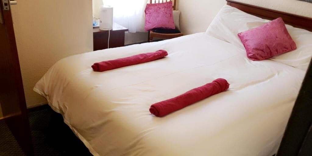 Cama bem arrumada com lençóis brancos e duas toalhas vermelhas.