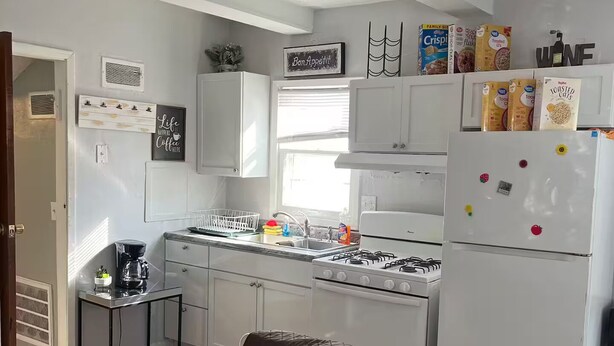 Cocina compacta con estufa a gas, armarios blancos y refrigerador.