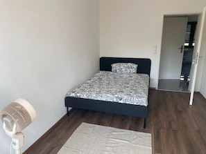 Ein Schlafzimmer mit einem Bett, einem Standventilator und einem Teppich.