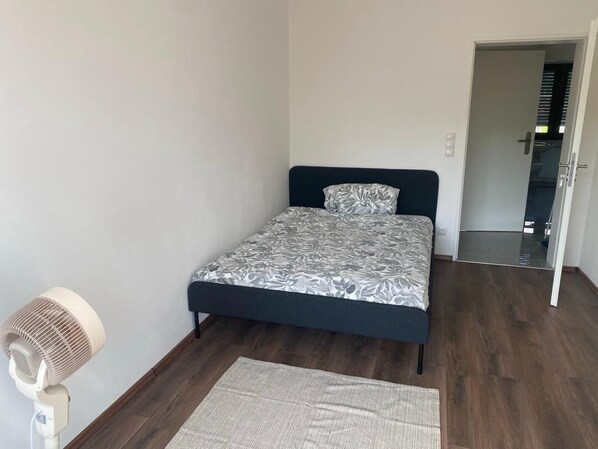 Ein Schlafzimmer mit einem Bett, einem Standventilator und einem Teppich.