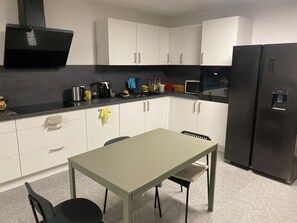 Eine kleine Küche mit weißen Schränken, einem schwarzen Kühlschrank, einem Esstisch mit Stühlen und einer Mikrowelle.
