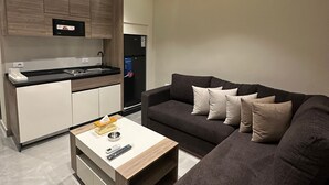 Een moderne woonkamer met een donkergrijze bank, een witte salontafel, en een keukenhoek met houten kastjes en een ingebouwde televisie.