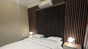 Een moderne hotelkamer met een groot bed, een nachtkastje met een lamp, een airconditioner en een wandpaneel.
