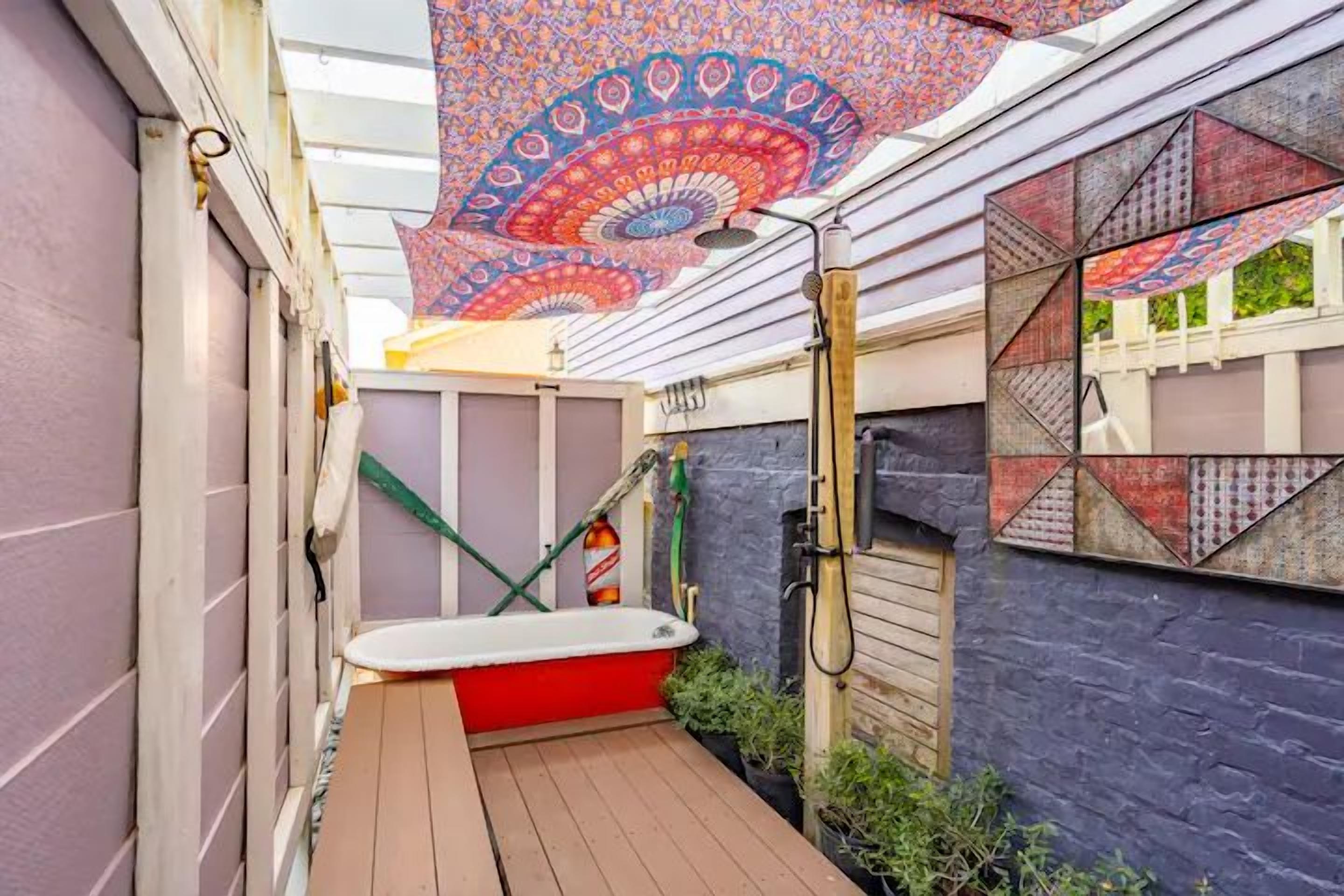 A sunroom with a patterned ceiling, a wooden deck, and a red bathtub.