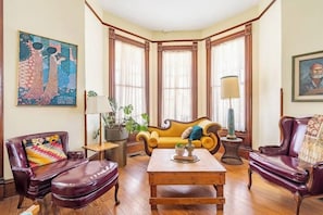 A room with a wooden coffee table, two leather armchairs, a yellow sofa, and a large painting on the wall.