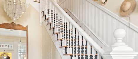 A staircase with white balusters and a white handrail, leading to a landing with a bench and a mirror.