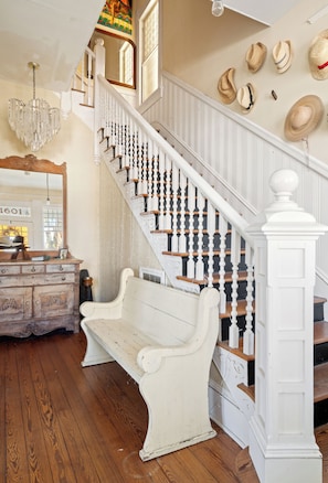 A staircase with white balusters and a white handrail, leading to a landing with a bench and a mirror.