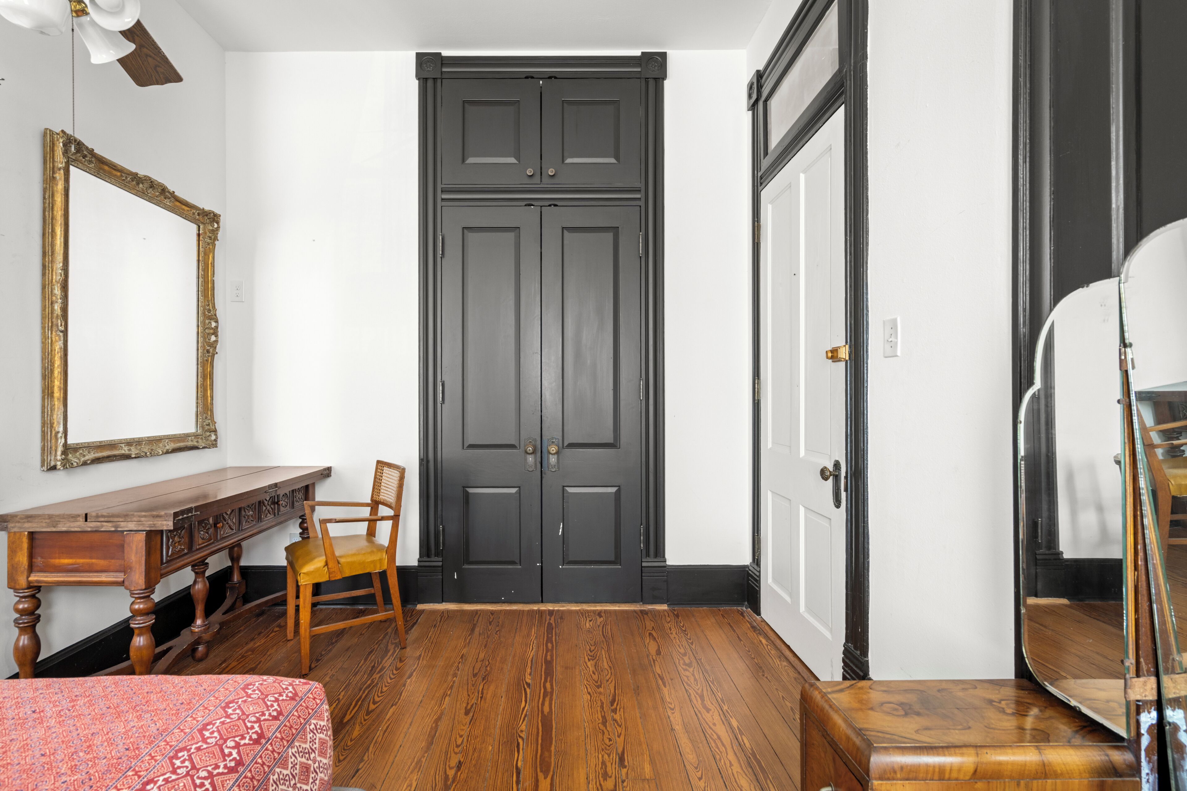 Une pièce avec un plancher en bois, un bureau avec une chaise, un grand miroir et une porte sombre.