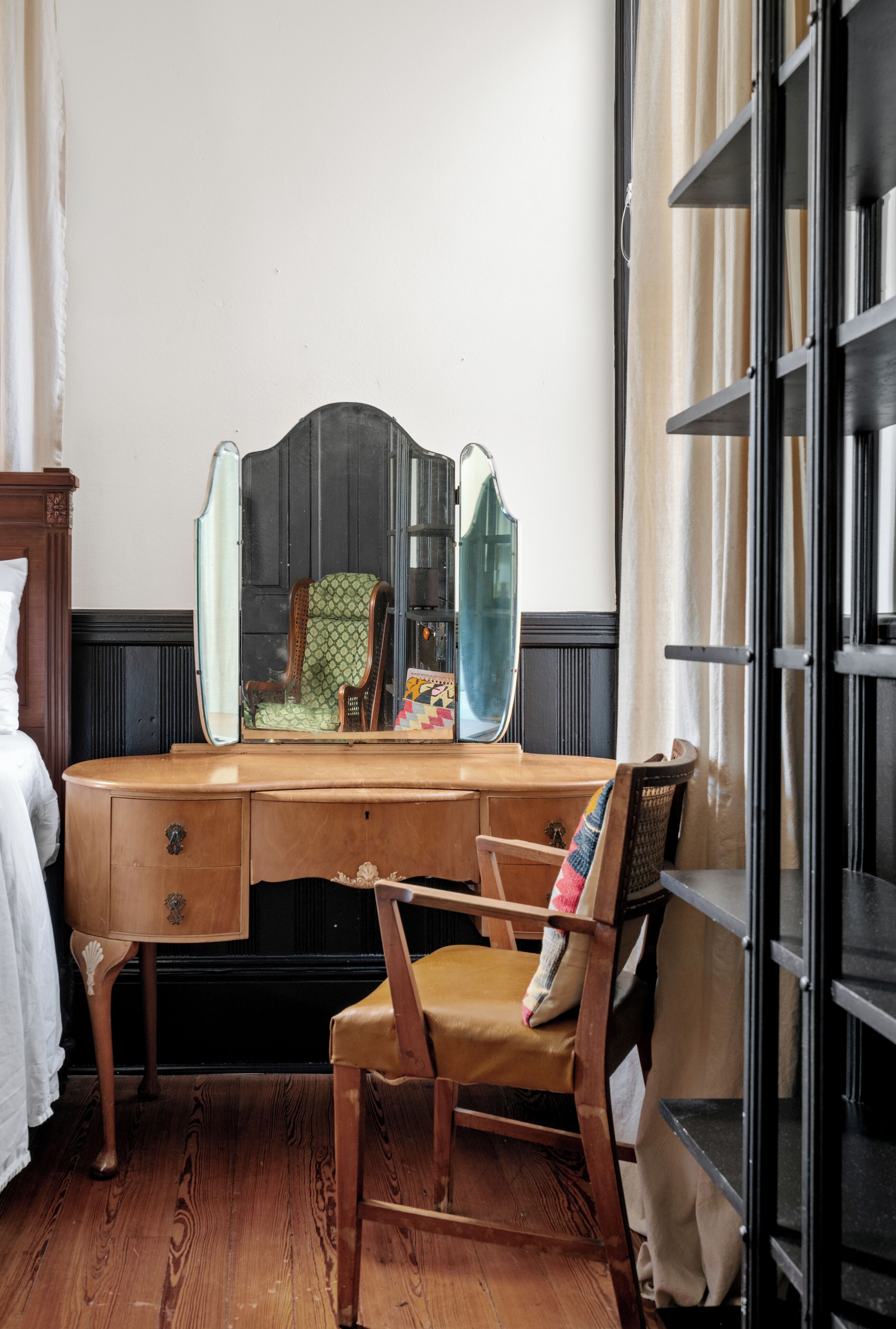 A wooden desk with a mirror, a chair, and a bookshelf.
