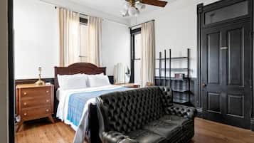 A bedroom with a bed, a black leather sofa, a wooden nightstand, a ceiling fan, and a black door.