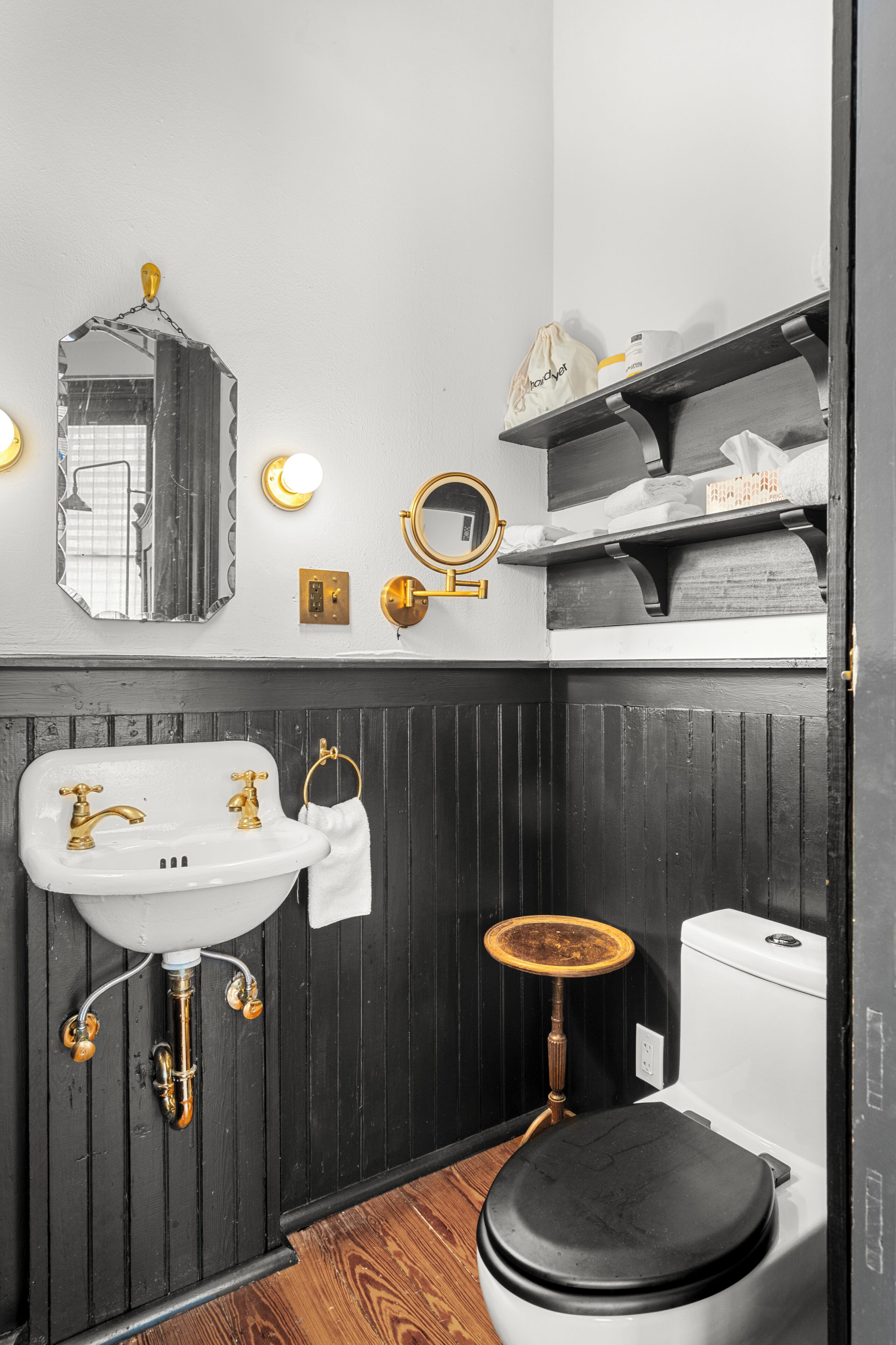 A bathroom with a white sink, gold fixtures, a round mirror, and a black toilet.