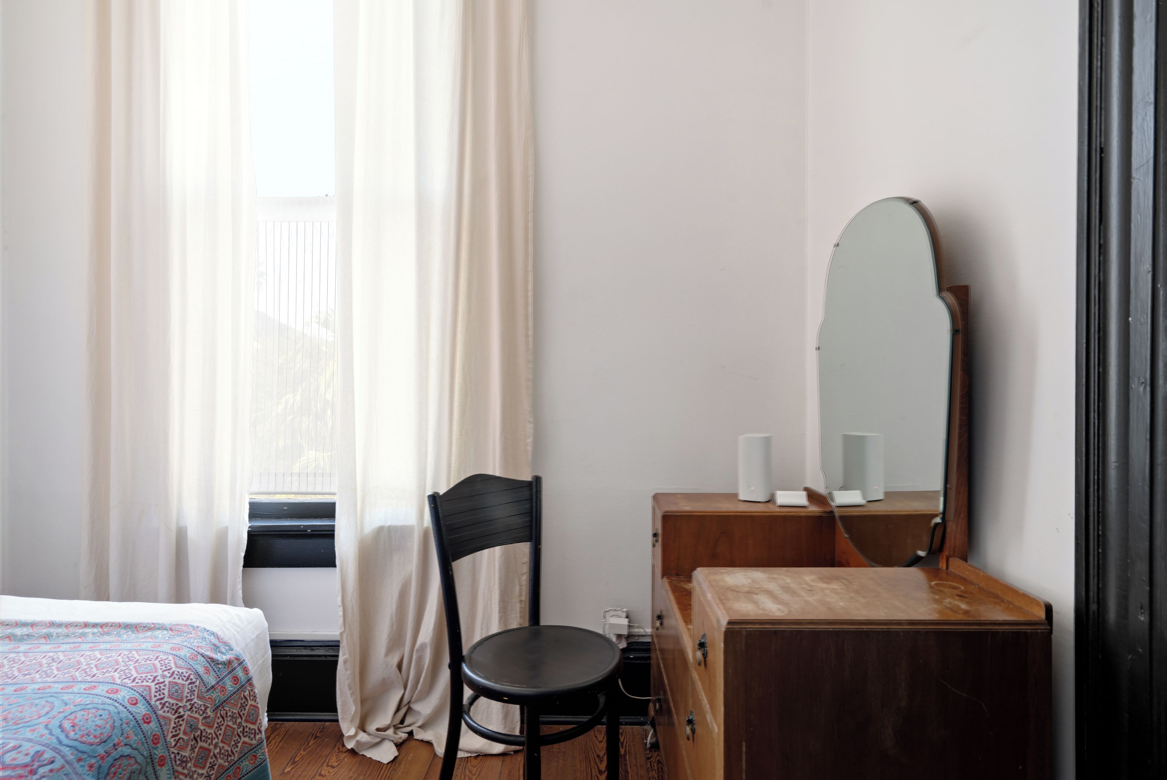 Ein Hotelzimmer mit Bett, einem Holzschrank, einem Sessel, einem Spiegel und einem Vorhangfenster.