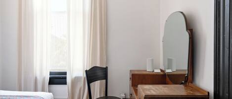 Ein Hotelzimmer mit Bett, einem Holzschrank, einem Sessel, einem Spiegel und einem Vorhangfenster.