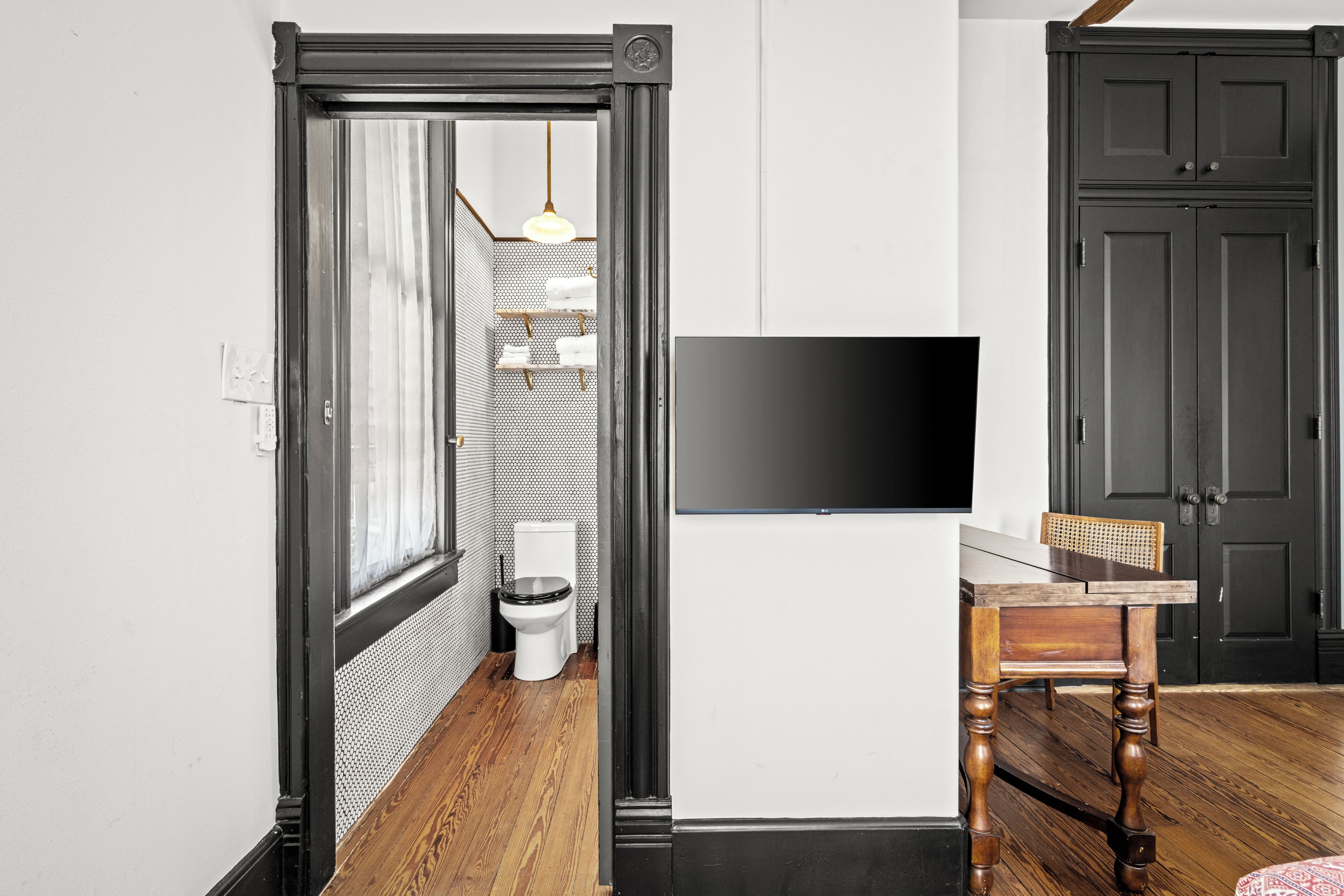 Un pasillo con suelo de madera, una puerta negra, pared blanca y un televisor montado.