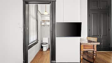 Un pasillo con suelo de madera, una puerta negra, pared blanca y un televisor montado.
