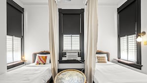 Quarto de hotel com duas camas, uma mesa redonda e uma janela com cortinas.