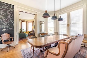 A dining area with a large wooden table, upholstered chairs, pendant lighting, and a chalkboard with writing. - St Helen s House Historic District  (Galveston)