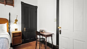 A room with a bed, a nightstand, a desk with a chair, a black door, and a white door.